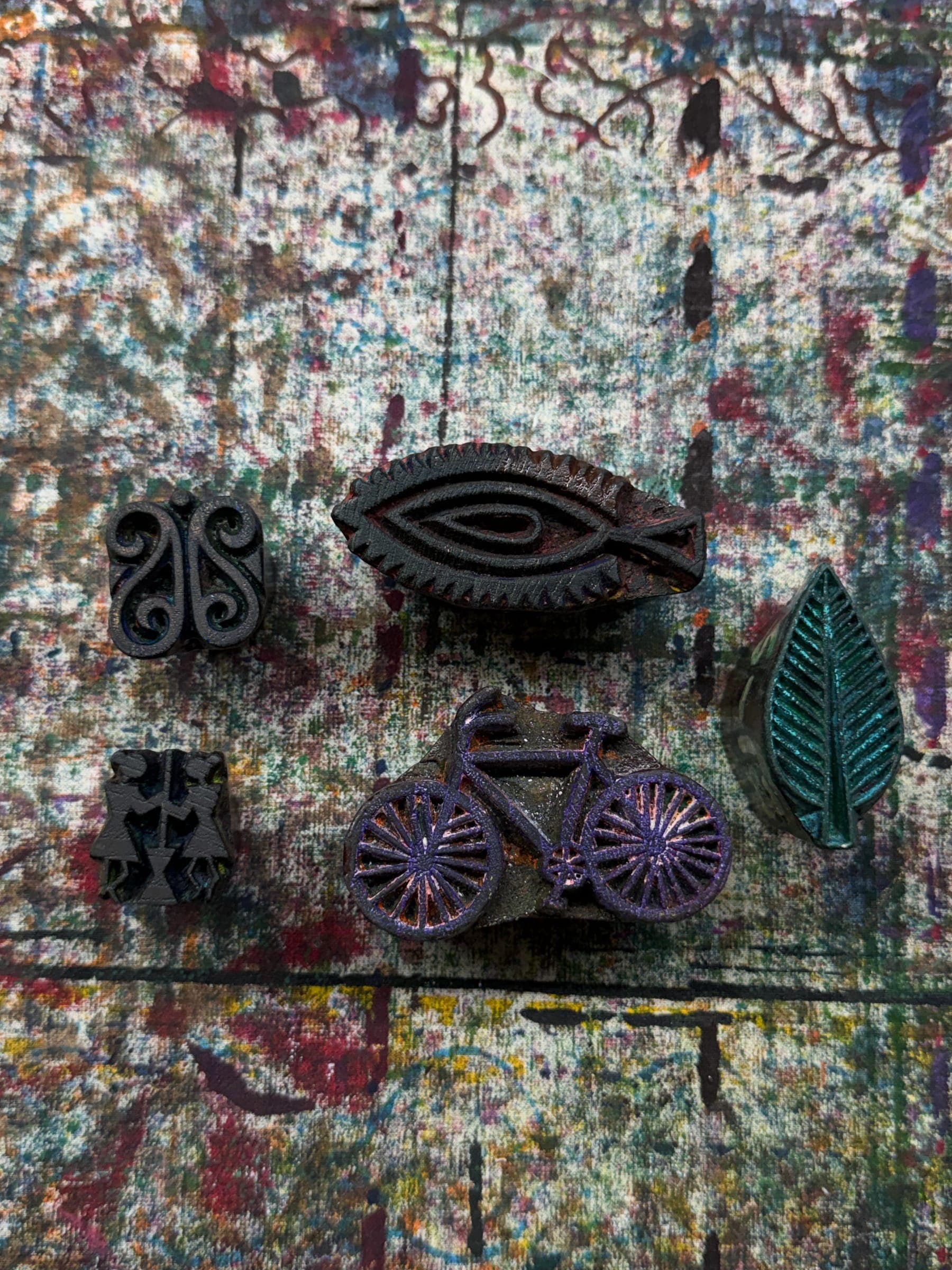Carved wooden printing blocks on the paint-mottled studio table, among them a bicycle, a leaf and a fish-eye motif