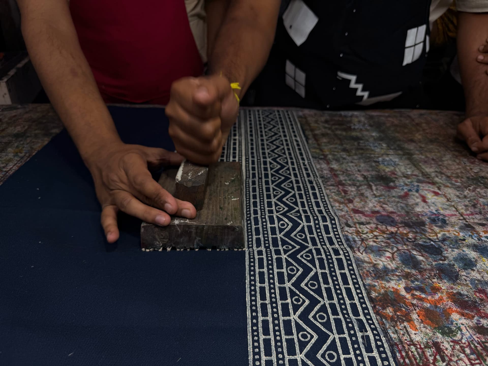Hands press a long carved block to continue a white geometric border across navy cotton
