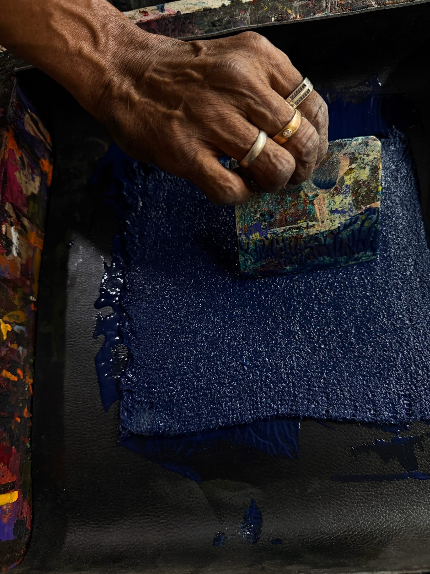 A ringed hand works a carved block through the indigo ink tray before printing