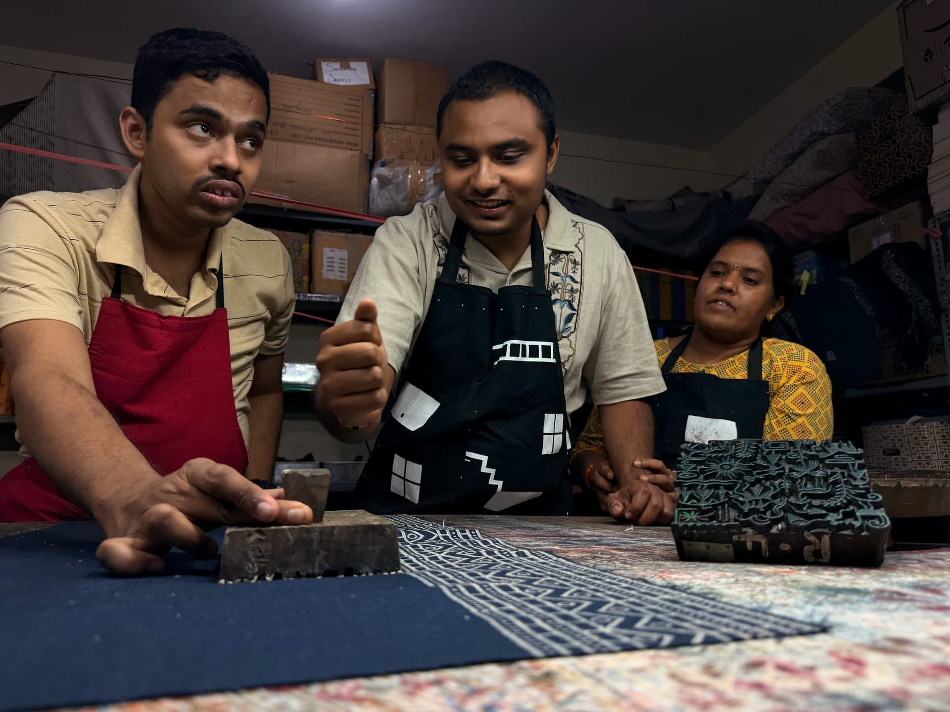 Three makers at the studio table printing an indigo border, carved blocks stacked beside them