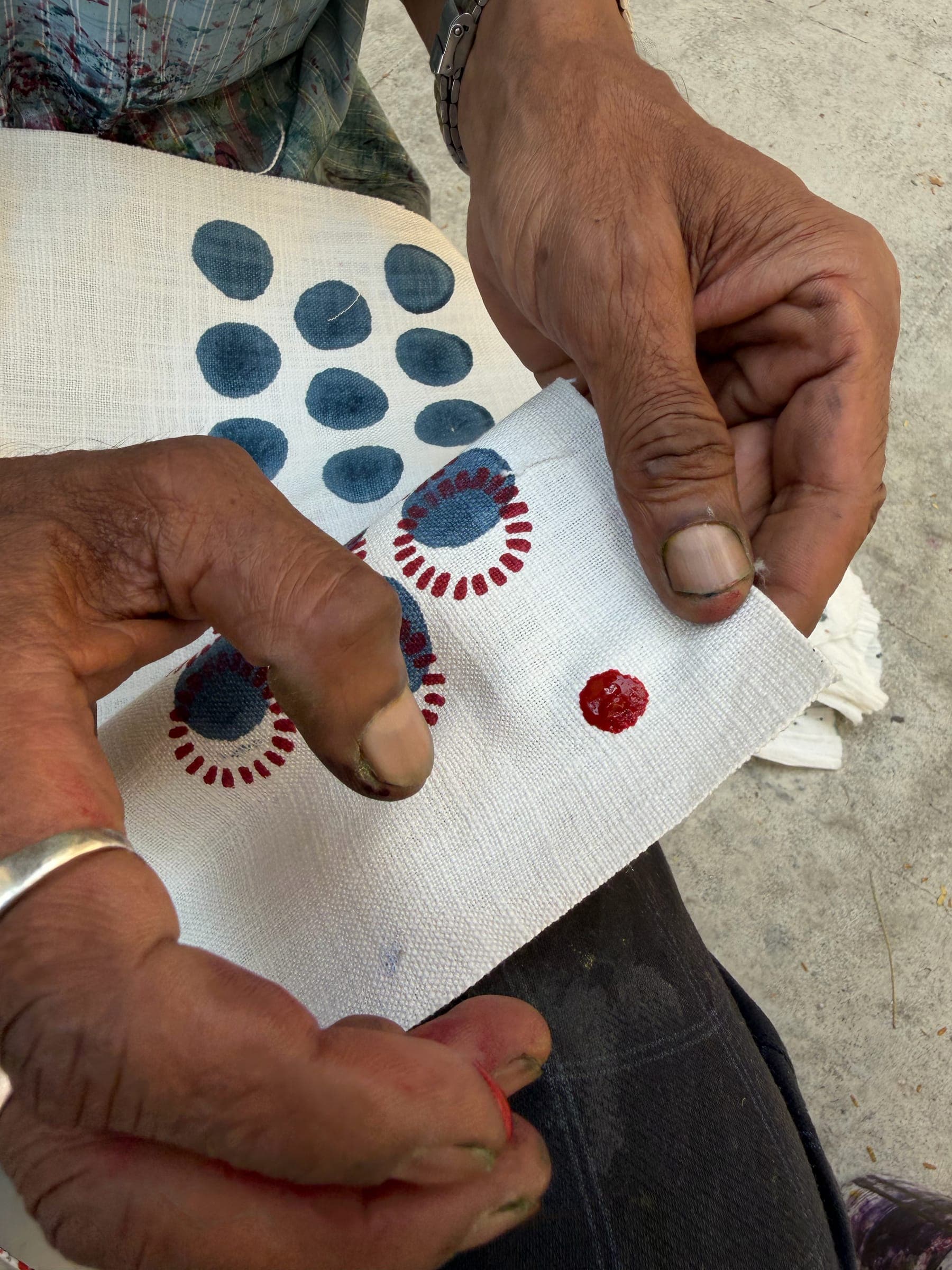A maker's hands place a freshly printed dot motif among a set drying on white cotton