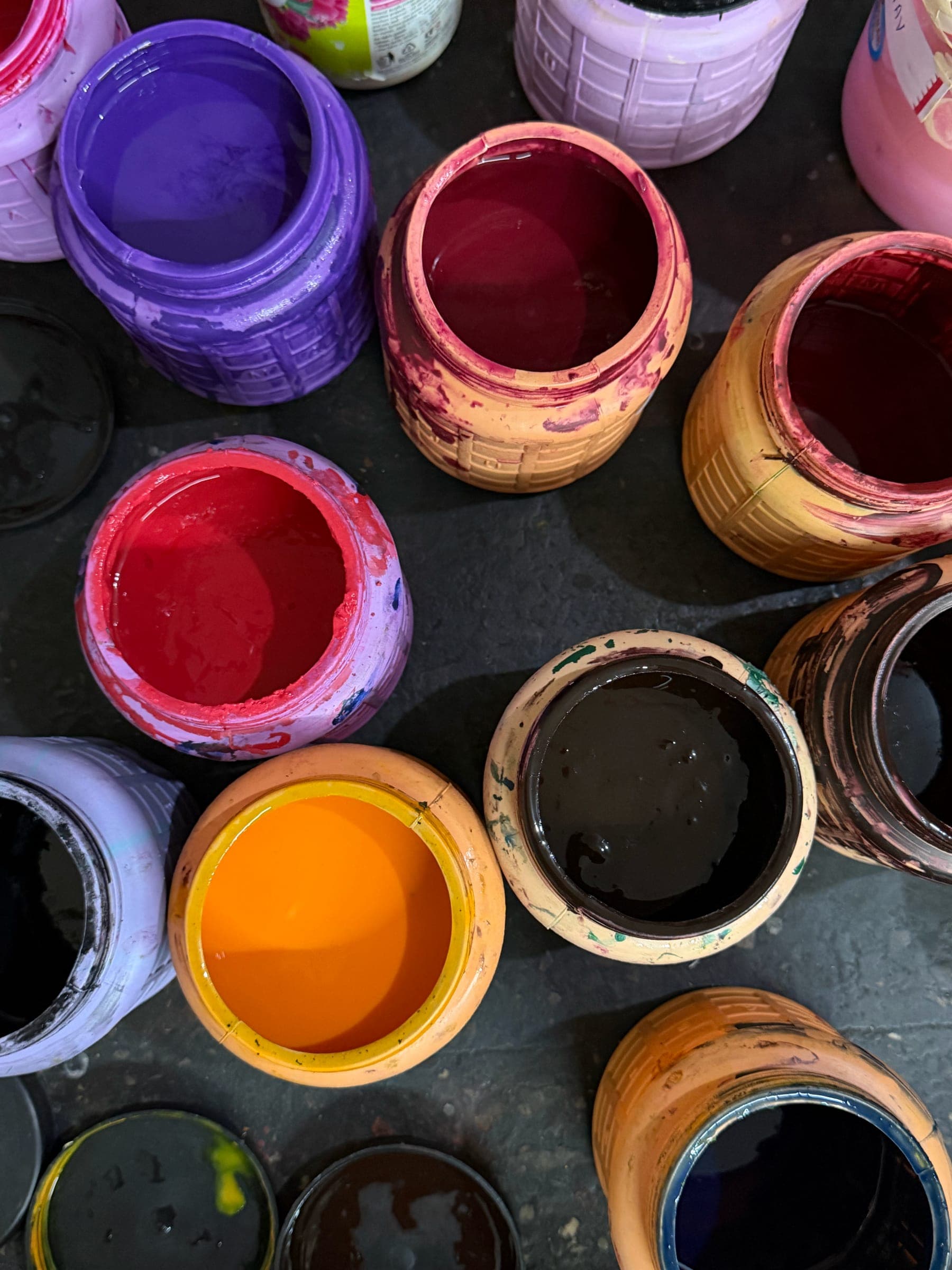 Open pots of fabric paint in purple, crimson, orange and black, seen from above on the mixing table